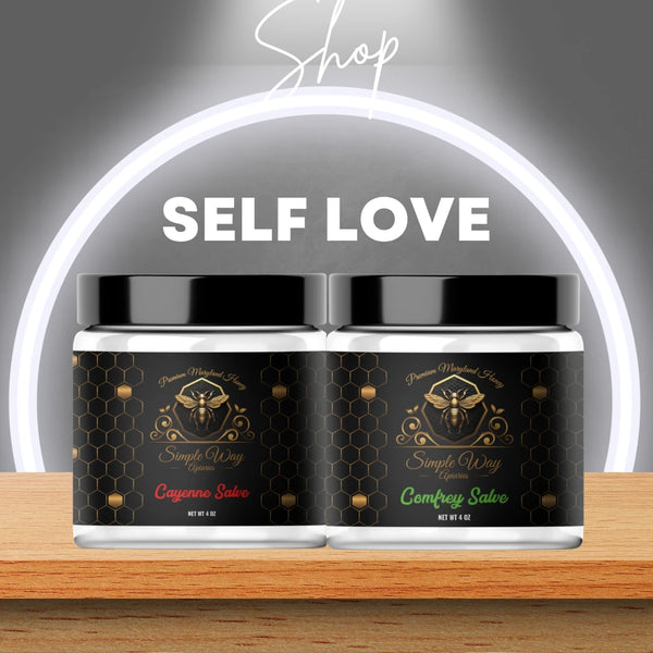 Simple Way Apiaries' Self-Love Salve Collection: Comfrey and Cayenne Salves displayed with fresh comfrey leaves and cayenne peppers on a rustic surface. Elegant jars with branded labels highlight their natural, healing properties and authenticity.